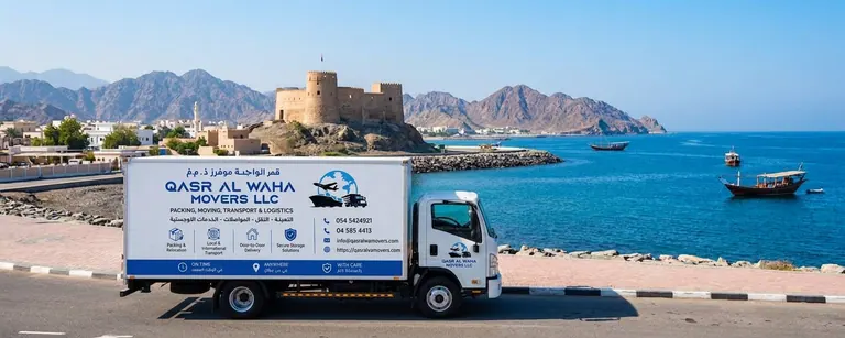 A Qasr Al Waha Movers truck on the Fujairah coast below a hilltop fort, with dhows at anchor