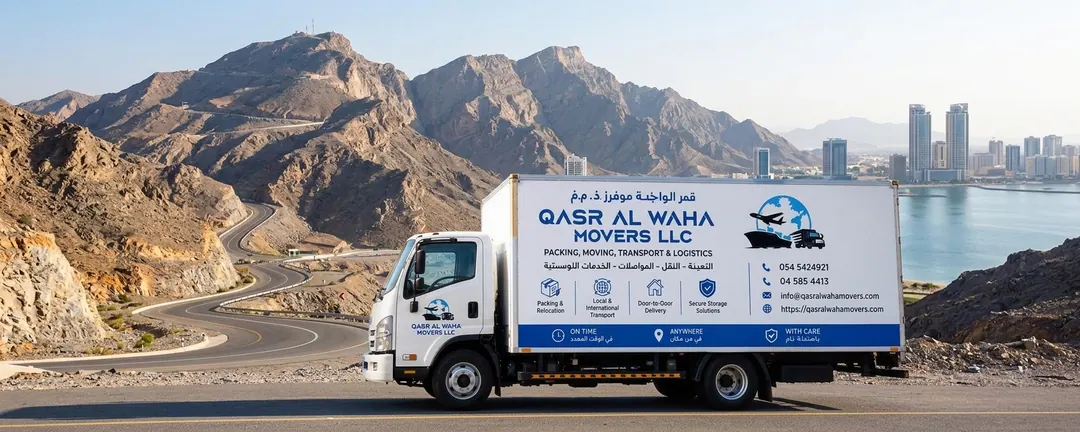 A Qasr Al Waha Movers truck on the mountain road above Ras Al Khaimah, with the city and coast beyond