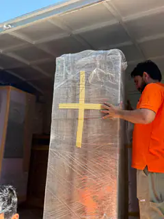 A mover stretch-wrapping a tall cabinet and taping it with a protective cross