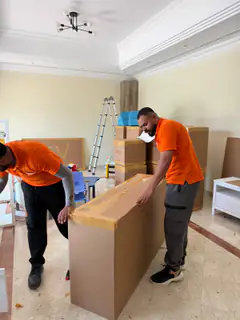 A mover taping a large wrapped item, with a step ladder behind