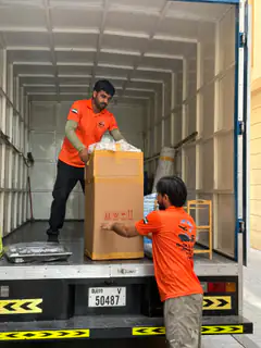 Two movers lifting a tall carton into a container