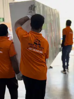 Movers carrying a wrapped upright item along a villa corridor
