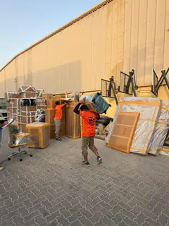 A mover carrying a chair past stacked packed goods