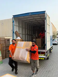 Two movers carrying a large wrapped item to the truck
