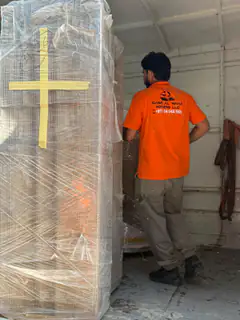 A mover finishing the wrap on a tall item against a wall
