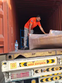 Two movers positioning a long wrapped item inside a container