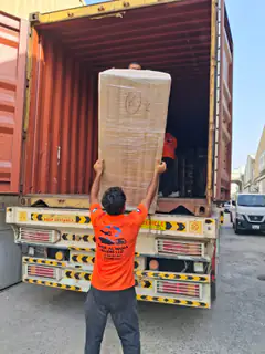 A mover lifting a wrapped mattress at the container door