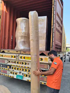 A mover standing a tall wrapped item up at the container door