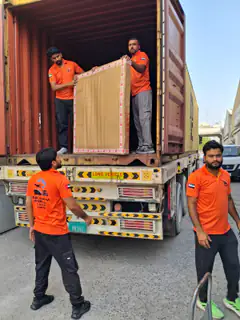 Two movers lifting a large carton into a container